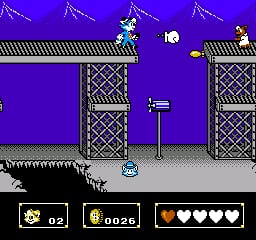 A blue cat character stands on gray ground in the center of a purple-tinted level. Two tall stone towers with cross-hatched patterns flank the sides, each topped with a small character figure. A white ball floats in the upper center. The HUD at the bottom displays a lives counter (02), a score display (0026), and a four-heart health bar. The background shows a repeating diagonal lightning bolt pattern against a vibrant purple sky.