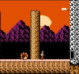 A platformer level features a tall golden tower in the center against an orange sky with purple mountainous terrain below. A small armored character stands on tan-colored ground to the left of the tower, with a small red enemy sprite nearby. The right edge shows a checkered pattern border. Purple mountain silhouettes form the background with a beige moon visible in the upper portion. The level uses a limited pixel-based NES-era color palette with solid orange sky, black shadows, and detailed 8-bit sprite work throughout.