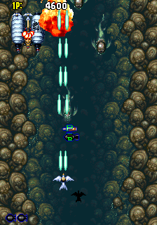 A vertical scrolling shooter viewed from above displays a narrow waterway bordered by brown rocky terrain. Three enemy aircraft formations composed of cyan and white sprite pixels occupy the upper and middle portions of the screen. A blue player aircraft sits centered near the bottom. The score reads 4600 in the upper right corner, with time remaining shown as 18 in the upper left. Two small UI icons appear in the lower left corner. The color palette consists primarily of greens, blues, browns, and grays with 16-bit sprite resolution typical of early 1990s arcade hardware.