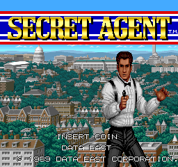 The title screen displays the large yellow "SECRET AGENT" logo at the top with red and blue horizontal stripes. A man in a white suit and black pants stands center-right, gesturing with one hand raised. Behind him stretches a wide cityscape rendered in isometric perspective with buildings, towers, and urban architecture in green and tan tones. At the bottom, white text reads "INSERT COIN" on the left, "FOR CREDITS" in the center, and "1989 DATA EAST CORPORATION" aligned right. The arcade instruction panel is visible at screen bottom.