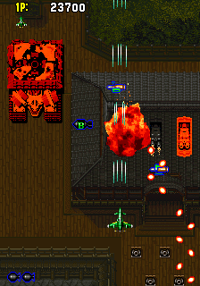 A top-down vertical scrolling shooter displays a player aircraft at bottom center firing upward at enemy formations and large explosive bursts. The playfield shows wooden and dark tiled terrain with orange explosions scattered across the screen. Two large red enemy sprites occupy the left and center areas. A score counter reads 23700 at top left, with ammunition indicators at bottom. Multiple green vertical projectiles and orange flame effects fill the middle section. The color palette emphasizes reds, oranges, and blacks against brown wood textures.