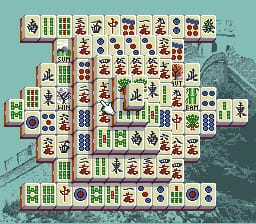 A mahjong solitaire puzzle board displays tiles arranged in a complex stacked pattern against a light turquoise background. The layout features bamboo, character, and dot tiles along with flower and season tiles, with a stone dragon statue visible in the bottom-right corner. The tile arrangement forms an asymmetrical shape with multiple levels, and a few tiles show highlighted selection states. The sprite resolution and color palette are typical of early 1990s SNES graphics.