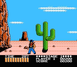 A pixelated desert scene features a blue sky with white clouds, brown rocky terrain, and a tall green cactus in the center. A character sprite stands in the lower-left area facing the cactus. The HUD displays "SHOOTING RANGE" at the top in yellow text, with a score counter showing "21" and "STAGE 1" and "BLOCK" indicators. Additional numerical readouts appear in the upper right. The sprite-based graphics use a limited color palette typical of NES-era games.