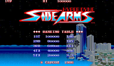 The title screen displays "SIDE ARMS" in large red and white pixelated letters at center, with "HYPER DYNE" text above it. Below the logo is a ranking table showing five high score entries with point values ranging from 100000 to 20000, each labeled with three-letter initials and difficulty indicators (L.GR, T.GR, M.GR, H.GR, N.GR). A cityscape with tall buildings and blue tones occupies the right side of the screen. At the bottom, "© CAPCOM 1986" appears in red text. The background is black with small white dots suggesting a starfield. The overall aesthetic is typical of mid-1980s arcade graphics with limited color palette and sprite-based design.
