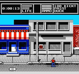 A skateboarding character in red stands on a city street at ground level, facing a multi-story building with white walls and dark windows. The HUD displays a timer reading 0:00:13 at the top left, with life meter and score indicators visible in the upper right corner. A striped storefront with blue awning appears on the left side. The background shows colorful buildings in red and blue tones with a bright cyan sky. The sprite-based graphics use typical NES resolution and limited color palette.