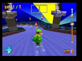 A character in bright green clothing rides a snowboard down a blue slope in a nighttime mountain setting. Two stone tower structures frame the track on either side. The HUD displays a lap counter reading 1/3 in the upper left, a life meter showing 100 at the bottom right, and the character position indicator 4 in the lower left. Yellow and light-colored geometric shapes represent buildings or structures in the distant background against a dark sky. The game uses flat-shaded 3D polygon graphics typical of Nintendo 64 rendering.