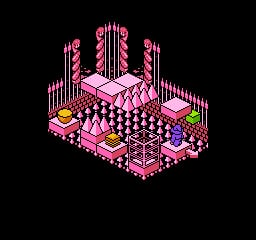 An isometric view displays a pink and magenta checkered floor pattern forming a square arena, bordered by tall vertical striped pink structures on all four sides. Small colored blocks in yellow, green, and red sit on the edges of the platform. The entire scene uses a limited pastel color palette rendered in low-resolution pixels against a black background, characteristic of early 8-bit isometric graphics.