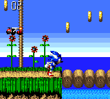 Sonic stands in the center-left of a colorful side-scrolling level with a bright blue sky, palm trees, and sand terrain. Golden ring clusters float in the air above. A green grassy platform with brown soil sits in the foreground, transitioning to blue water below. The HUD displays a red life counter and score in the upper-left corner. The sprite-based graphics feature 8-bit pixel art with vibrant primary colors and distinct layered parallax elements creating depth.