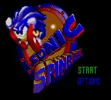 Sonic the Hedgehog appears in the center of the screen in a blue spherical form, surrounded by red and brown mechanical structures resembling a pinball machine environment. The word "START" is displayed in green text in the lower right corner, with "SONIC" visible below it in blue. The background is solid black, and the sprite-based graphics use a limited color palette typical of Game Gear hardware, showing pixelated details of the character and metallic pinball machine elements.