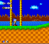 Sonic stands on a green grass platform in the center-lower portion of the screen, facing right. A blue sky with cyan cloud formations fills the upper half. A tall brown tower or structure rises from the ground behind Sonic. The HUD displays 01:45 and 0000 in the top-left corner in white text. Brown checkered platforms form the bottom layer. The sprite-based graphics use a limited color palette typical of Game Boy Color hardware, with distinct pixelated character and environmental sprites.