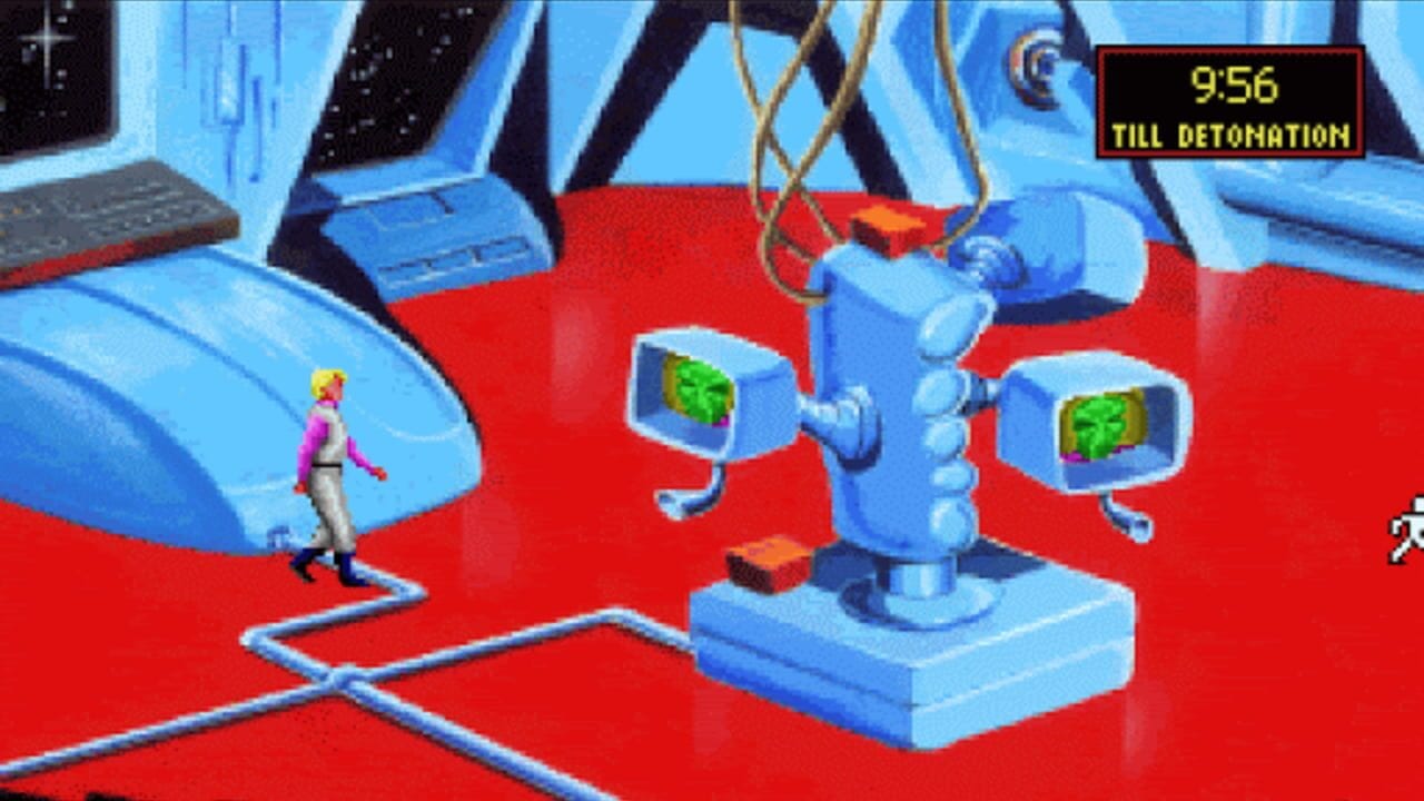 A character in white and magenta clothing stands on a blue platform within a red chamber. Behind the character, a blue robotic arm with multiple segments holds two small cubes displaying green digital faces. Additional blue mechanical structures and equipment line the upper portion of the space. The top-right corner displays a yellow text timer reading '9:56 TILL DETONATION' against a black background. The environment features isometric perspective with blue and red color blocking, typical of early 1990s VGA graphics.