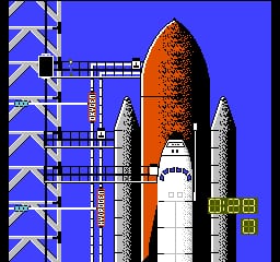 A space shuttle on the launch pad dominates the center of the screen, rendered in orange and white pixels against a bright blue background. Four tall gray booster rockets flank the shuttle on either side. On the left edge, a vertical stack of blue and white checkerboard-patterned launch tower segments extends from top to bottom. In the lower right corner, white numerical displays show "828" and "0", likely indicating score and lives remaining.