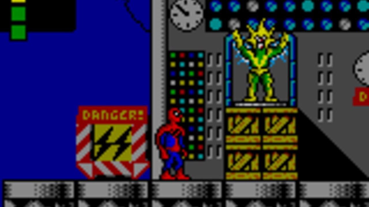 A side-scrolling platformer scene shows a red-costumed character standing in a gray industrial corridor with yellow striped warning panels and metal scaffolding. A large yellow and green villain sprite looms in the center-right background on an elevated platform. The left side displays a red danger warning sign with yellow chevron stripes. A colorful dot-matrix style panel with cyan, yellow, and green pixels occupies the upper-left area. Gray metallic grating and circuit-board patterns fill the floor. The scene uses bright primary colors against dark backgrounds with low-resolution pixel art typical of early handheld gaming.