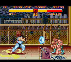 Two fighting game characters face off in a street-level arena with a chain-link fence backdrop and storefronts visible behind it. The left character wears white and blue clothing in a crouching stance, while the right character in red and white sits in a flower-decorated chair. A horizontal score display spans the top of the screen showing health bars, round number, and time remaining in yellow and red text against a dark background. The sprite artwork displays the characteristic pixel resolution and color palette typical of 16-bit fighting game graphics.