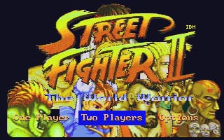 The title screen displays the Street Fighter II logo in large yellow and orange letters at the top, with the subtitle 'The World Warrior' below. Character portraits line the bottom, including a bearded man on the left and a stern-faced man on the right. A blue menu bar in the center presents options including 'Two Players' in white text. The background is dark navy with gradient shading and character artwork. Low-resolution sprite graphics typical of early DOS ports are visible throughout.
