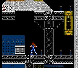 The protagonist Strider stands on a metal platform in the center of a dark industrial interior. A yellow cargo container hangs from a chain mechanism at upper right. Blue textured floor panels occupy the lower left corner. The HUD displays score values in the upper left. The scene features black backgrounds, gray steel girders forming a cross pattern, and 8-bit sprite-based graphics typical of NES-era action games.