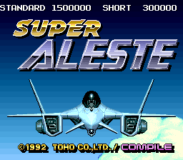 The title screen displays "SUPER ALESTE" in large metallic blue lettering against a dark blue gradient sky. A white fighter jet with twin engines is centered prominently below the title. The top of the screen shows game mode options: "STANDARD 1500000 SHORT 300000" in white text. At the bottom, copyright text reads "©1992 TOHO CO.,LTD./COMPILE" in yellow and blue lettering. The background features a light blue sky with white clouds, creating a clean, minimalist layout typical of early 1990s shoot-em-up title screens.