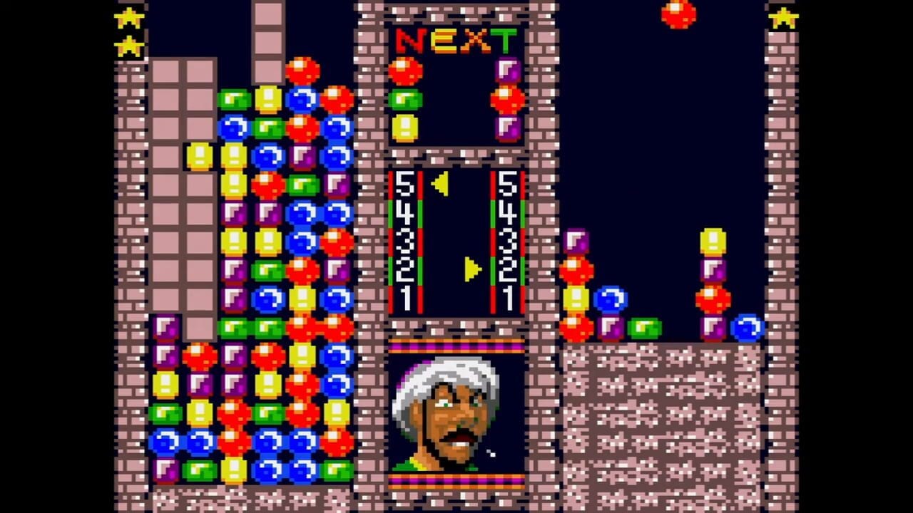 A match-three puzzle game displays two active play areas with colored blocks (red, blue, yellow, green, purple) stacked in vertical columns against brick-textured walls. The upper "NEXT" panel shows upcoming pieces, while the lower play field shows score counters reading 5453 and 5453 with vertical markers. Two yellow stars appear in the top corners, and a character portrait with white hair and mustache is visible in the lower-left corner. The overall aesthetic features 16-bit pixel art with a dark blue background and ornate brick framing around the game areas.