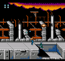 A soldier in dark armor runs rightward along a gray platform in an industrial factory setting. Brown metal scaffolding and machinery towers above, with orange-yellow fire and explosions visible in the background sky. Blue water or liquid pools appear in the lower right corner. Gray and brown brick structures line the base of the scene. Small white UI elements display in the top left corner. The 8-bit pixel art uses a limited color palette of oranges, browns, grays, and blues against a black background.