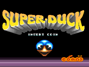 The title screen displays "SUPER DUCK" in large yellow pixelated letters with a 3D shading effect against a black background. Below the title, white text reads "INSERT COIN". A gold and blue pixelated duck face with wide eyes and an open beak is centered in the middle of the screen. The Comad developer logo appears in the bottom right corner in orange and red text. A purple horizontal bar runs across the lower portion of the screen.