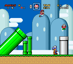 A side-scrolling platformer level displays Mario standing on tan ground in the lower-left area, facing right toward a green warp pipe. Blue-gray castle structures with white circular windows fill the background, and a large green diagonal pipe extends from the upper-left. The HUD shows score at top-left, time counter at center-top, and lives/item icons at top-right against a bright blue sky. Two small red enemies appear in the middle-right distance near the castle architecture. The sprite-based graphics use a 16-bit color palette with parallax layers creating depth.