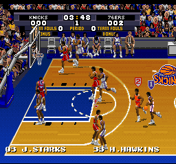 A basketball court in isometric perspective shows two teams during active play. The U.S. Starters team in blue jerseys faces off against a team in red jerseys. A scoreboard at the top displays team names, quarter information (002), and scores. Players are positioned across the court in varied stances, with the ball visible in play. The court features blue sidelines and paint against a tan floor. Pixel art sprites represent each player, rendered in the SNES's 16-bit color palette. A crowd of spectators appears in the background bleachers.