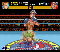 A boxing ring viewed from above shows a shirtless fighter in blue shorts positioned below an opponent with pink/red skin and blonde hair in the center of the ring. The round number and fight timer display at the top, with a yellow health bar beneath showing the player's remaining health and a similar bar for the opponent. Red crowd sprites fill the background bleachers around the ring, rendered in low-resolution 16-bit sprites against a light blue canvas. The ring floor features diagonal stripe patterns in red, white, and blue.