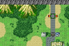 A top-down tactical battle map displays a green landscape with tan-colored forest clusters and a gray paved road running vertically through the center. Two mecha units are positioned on the road—one blue unit near the top and one purple unit below it. A small building structure appears in the lower-left corner. The scene uses GBA-era 16-bit sprite graphics with a limited color palette of greens, tans, grays, and metallics typical of early 2000s tactical RPG interfaces.