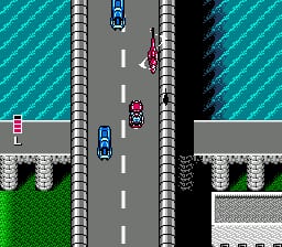 A top-down view of a multi-lane highway with turquoise water visible on both sides. A player vehicle in white occupies the center lane, while two enemy vehicles in red and blue are positioned ahead. Gray concrete barriers line the road's edges, with green grass terrain and gray building structures visible in the corners. A white dashed center line divides the road, and the sprite-based graphics display the characteristic pixelated style of early-1990s NES gameplay.