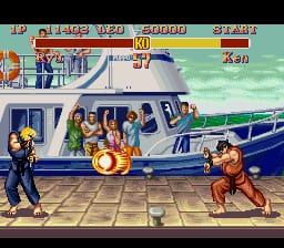 Two pixelated fighters stand facing each other on a tiled street in front of a blue airplane fuselage. The left character wears dark clothing and has a yellow aura, while the right character in brown executes an orange-flamed attack. A horizontal HUD bar spans the top displaying both fighters' health bars in red and blue, round number, timer, and win count. The background shows a light blue sky with green ground and aircraft details rendered in 16-bit SNES sprite graphics.