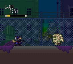 A side-scrolling level displays a blue-suited character in the lower-left corner on a brown ground platform, facing right toward enemy sprites clustered in the lower-right area. A diamond-pattern fence structure spans the middle of the screen with green and purple atmospheric elements. The HUD at top-left shows "L:00" and "3:51" in white pixelated text with a yellow progress bar. The visual style uses a limited 16-bit color palette with scrolling layered backgrounds in dark blue and purple tones typical of SNES-era sprite animation.