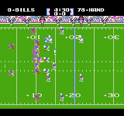 A football field viewed from above displays two teams of pixelated players lined up in formation across the yard lines. The top left shows score information reading '0-BILLS' with '43:39' and '78-HAND' displayed. White field markers and yard numbers are visible at 10, 20, and 30-yard lines. Players are rendered as small colored sprites arranged in offensive and defensive formations on the bright green field. The play appears to be set up with the ball near the center of the formation.