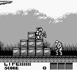 A monochrome Game Boy screenshot displays two anthropomorphic characters standing on a wooden platform against a gray mountainous background. The left character wears armor or combat gear, while the right character appears similarly equipped. Grass silhouettes line the bottom edge. At the top left, "LIFE:||||" and "SCORE" text indicate health and points, with the score shown as zero. The right side of the screen displays a row of inventory or status boxes. The pixel art uses the typical Game Boy's limited monochrome palette with clear sprite definition.