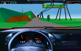 A first-person view from inside a car cockpit shows a blue steering wheel and dashboard with gauges and instruments. Through the windshield, a 3D landscape unfolds with rolling green hills, brown terrain, a blue sky, and an industrial structure with metal framework in the distance. The road stretches ahead with a striped texture pattern. The top of the screen displays a heads-up display with speed and gear information. The graphics use flat-shaded polygons typical of early 1990s racing game technology.