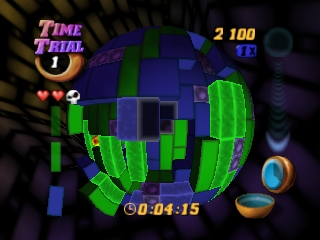A rotating 3D sphere dominates the center of the screen, covered in bright green and dark blue Tetris blocks arranged in various configurations. The upper left displays the "Time Trial" mode label with a gold circular icon and a life counter showing two full hearts and a partial third. The score reads 2100 in the upper right corner. A timer at the bottom center shows 00:04:15. Two UI elements appear on the right side: a small circular icon and a horizontal bar gauge. The background is dark with subtle geometric patterns.