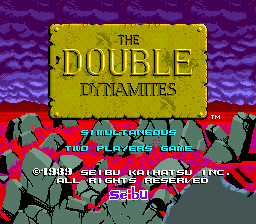 The title screen displays a large yellow rectangular banner reading 'THE DOUBLE DYNAMITES' in brown capital letters at the center. Below it, red text shows 'ONE OR TWO PLAYERS GAME' with a copyright notice for Seibu Kaihatsu Inc. from 1989. The background features a purple wavy pattern with red horizontal stripes at the bottom. Two gray pixelated robot or character sprites flank the title banner on either side. Purple and blue gradient effects create a striped visual backdrop.
