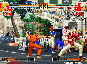 Two fighters in mid-combat on a street stage with palm trees and Mediterranean architecture in the background. The left fighter wears orange with blue trim, the right fighter in red and white. A crowd of blue-clothed spectators fills the background along white barriers. The HUD displays health bars for both fighters at the bottom, with a round counter and timer at the top showing "00" and "31". Pixel art sprites and stage elements rendered in 16-bit resolution with a scrolling parallax background showing detailed street scenery, market stalls, and spectator areas.