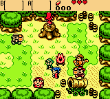 A top-down view of a grassy outdoor area with a brown-haired protagonist in the center wearing green tunic. Multiple enemies and NPCs are scattered across the verdant landscape, including sword-wielding adversaries and armored figures. A yellow score or status bar appears at the top displaying numbers and icons. The pixel art uses a bright green color palette for grass with brown earth patches, tan structures, and varied sprite designs typical of Game Boy Color graphics. Various interactive objects and terrain elements populate the environment in a grid-based layout.