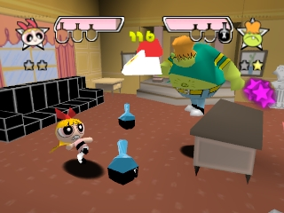 The Powerpuff Girls stand in a brown-floored living room interior with pink walls, a black couch, gray furniture, and potted plants. Health bars appear at the top left and right of the screen. Three blue cone-shaped enemies are positioned on the floor between the player characters and scattered furniture. A large green creature with pink accents hovers in the upper right. The graphics use 3D polygon models with a bright, saturated color palette typical of Nintendo 64-era games.