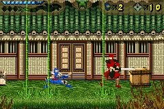 A red ninja character stands in the center-left of a side-scrolling level, facing a wooden storefront with closed doors and windows. The building features brown wood paneling and decorative architectural details. A blue barrel sits to the left of the character, and grass occupies the ground level. The background displays repeating green wooden fence panels with a yellow-green tiled roof structure above. The top UI shows two digit counters in the upper right corner. The sprite work uses a 16-bit pixel art style with distinct color separation between characters, objects, and environment layers.