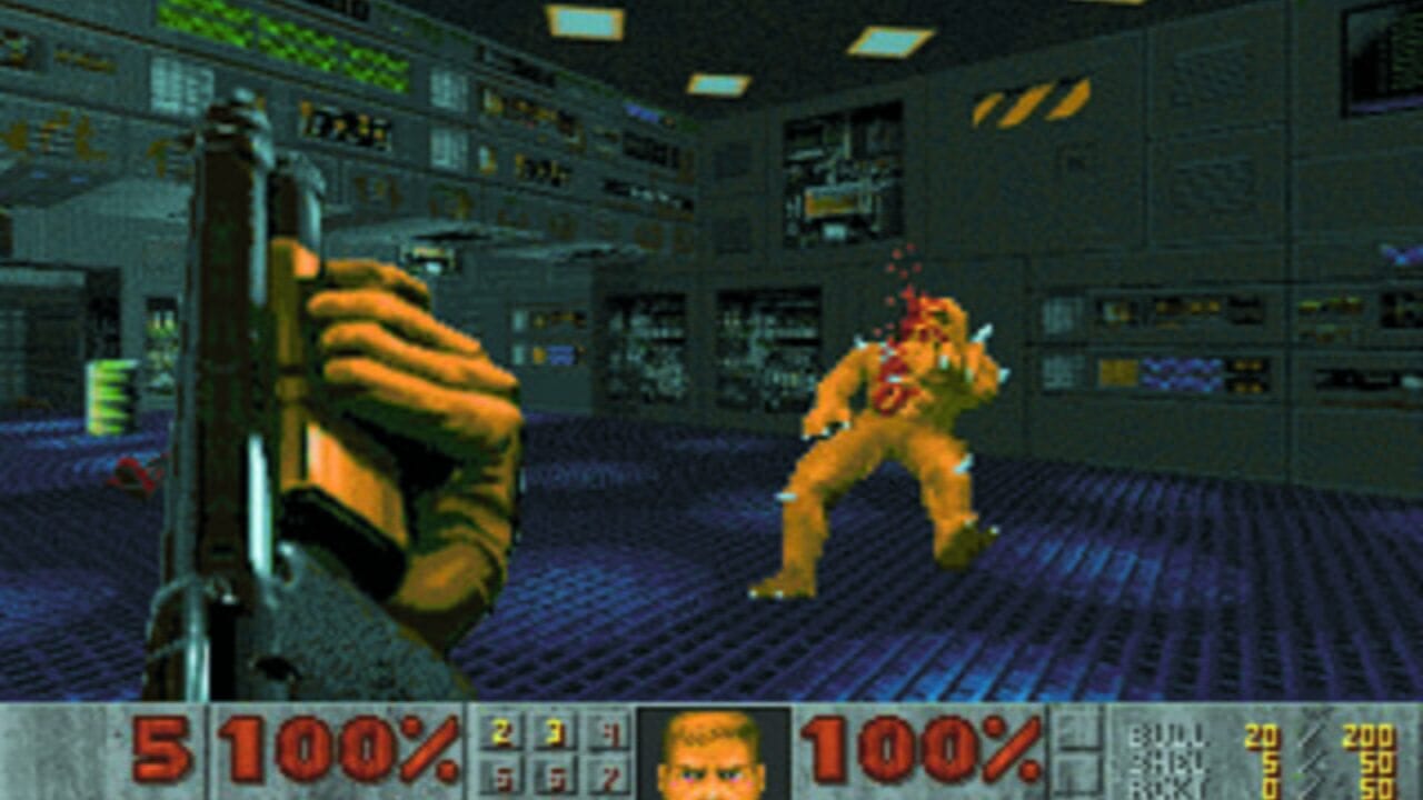 A first-person shooter view inside a dark industrial facility with gray walls and blue-ribbed flooring. A green-armored player character on the left holds a large yellow and gray weapon. An orange demonic enemy with red accents stands across the room in a combat stance. The HUD displays 100% health on both left and right sides, ammunition counts in the center, and a small portrait of the player character. Control panels with yellow and cyan lights cover the upper walls, and a yellow-striped warning symbol is visible on the right wall.