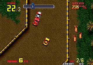A top-down view of a racing game in progress shows two red vehicles on a brown dirt track bordered by yellow lane markers and green grass. The HUD displays life at 22.3 in the upper left, speed 288 in the upper right, time 6 in the lower left, and laps 2/6 in the lower right. The player's car occupies the center-left of the screen while an opponent vehicle is visible ahead on the track. Sparse trees and obstacles appear on the grass verges on the right side.