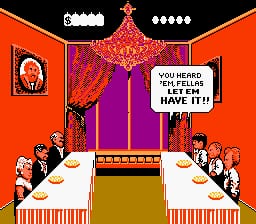 A dining scene with two long tables flanking a central stage area. Cartoon characters in formal attire sit at both tables facing inward. A large red curtain with gold trim hangs above the stage, with a chandelier suspended in front. The top of the screen displays a Cinemaware logo and score information. A speech bubble from a character on stage reads "YOU HEARD CORRECTLY, LET'S GO HAVE IT!" The background is solid orange-red, and the overall art style uses bright colors with thick black outlines typical of late-1980s NES graphics.