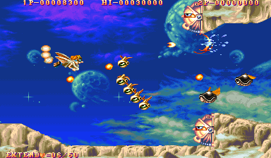 A vertical-scrolling arcade shooter depicts a blue sky level with rocky terrain at bottom and top edges. Multiple enemy aircraft in tan and brown colors fly across the screen in formation and scattered patterns. Golden projectiles from player weapons trail across the playing field. The HUD shows a yellow score counter at top-left reading 0-0008900, a health or power bar at top-center, and an additional score display at top-right. The sprite-based graphics use a 16-bit color palette with parallax cloud layering in the background.