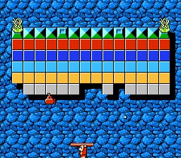 A blue brick background fills the screen with a horizontal platform structure in the center composed of four color-coded rows: green and yellow blocks at the top, red blocks in the second row, light blue blocks in the third row, and beige blocks in the fourth row. Small yellow icons appear at each end of the platform structure. A red character sprite stands in the lower center of the screen against the brick background.