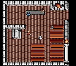 A top-down interior room view displays wooden crates and barrels arranged throughout the space. A small character sprite stands in the center area. The room features a decorative border frame with vertical white striping around the edges and brick-pattern walls in red-brown tones. A doorway or window opening appears in the upper left corner, and what appears to be a treasure chest or container sits against the left wall. The HUD shows a small icon in the upper right corner.