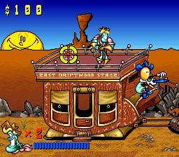 A western-themed shooter interface displays a large red and brown ornate train car as the central target in a sandy desert landscape. A cowboy character stands to the right holding a rifle, positioned to fire at the train. The sky is solid blue, and the scene uses bright primary colors with 16-bit sprite graphics. The score "$100" appears in the top-left corner, with a life counter showing in the bottom-left. The train car features two large circular windows and ornate wooden detailing against the flat, tan desert ground.