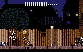 A platformer level displays a brown wooden fence spanning the width of the screen, with a fox character positioned on the left side. Behind the fence, a dark night scene shows a brick building with lit windows on the right, a black tree silhouette on the left, and blue sky above. A white dashed line and dotted UI elements appear at the top, indicating score or progress tracking. The pixel art uses a 16-bit color palette with detailed sprite animation for the character and environment.