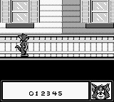 A Game Boy screenshot shows Tom the cat positioned on a wooden ledge or platform in the center of the screen, rendered in black and white monochrome pixels. Above are four window frames arranged horizontally across the top portion. Below Tom's current position stretches a horizontal beam or rail structure with a fence-like railing pattern. The bottom of the screen displays a score counter reading "01 2345" alongside what appears to be a small sprite icon on the right side. The background is predominantly black, characteristic of Game Boy's limited color palette.