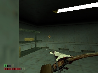 A first-person perspective showing a rifle held in the lower-right corner of the screen, pointing at a prone enemy soldier on a concrete floor inside a dark industrial interior. The room has metal railings, green-gray walls, and fluorescent lighting visible at the top. A health bar and ammo counter display in the lower-left corner. The scene uses N64-era 3D polygon graphics with flat-shaded surfaces and limited texture detail.